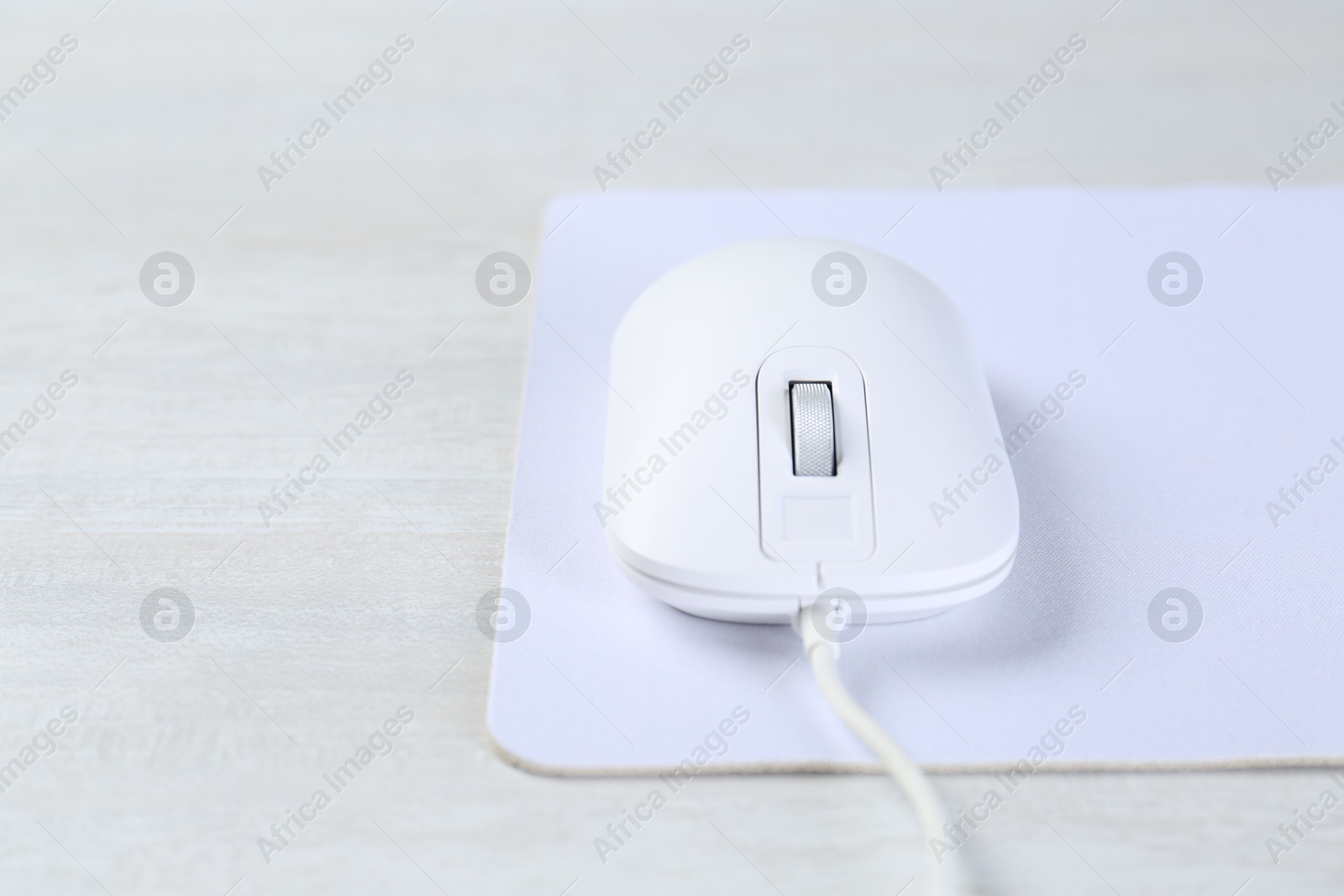 Photo of Computer mouse with mousepad on light wooden table, closeup