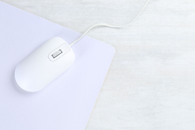 Photo of Computer mouse with mousepad on light wooden table, top view. Space for text