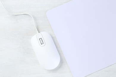 Photo of Computer mouse with mousepad on light wooden table, flat lay