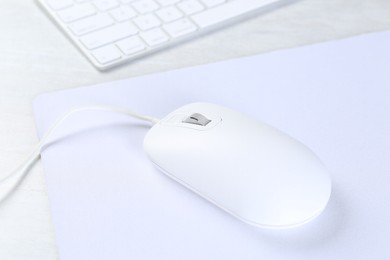 Photo of Computer mouse with mousepad and keyboard on light wooden table, closeup