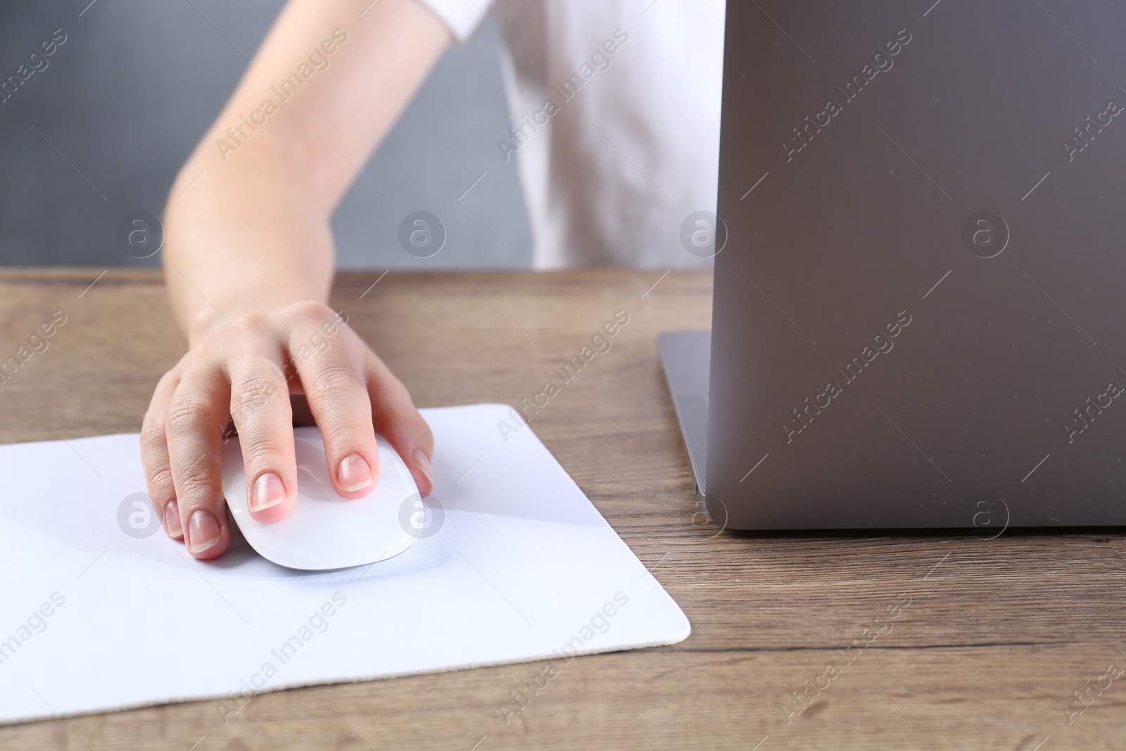 Photo of Woman using computer mouse while working with laptop at wooden table, closeup