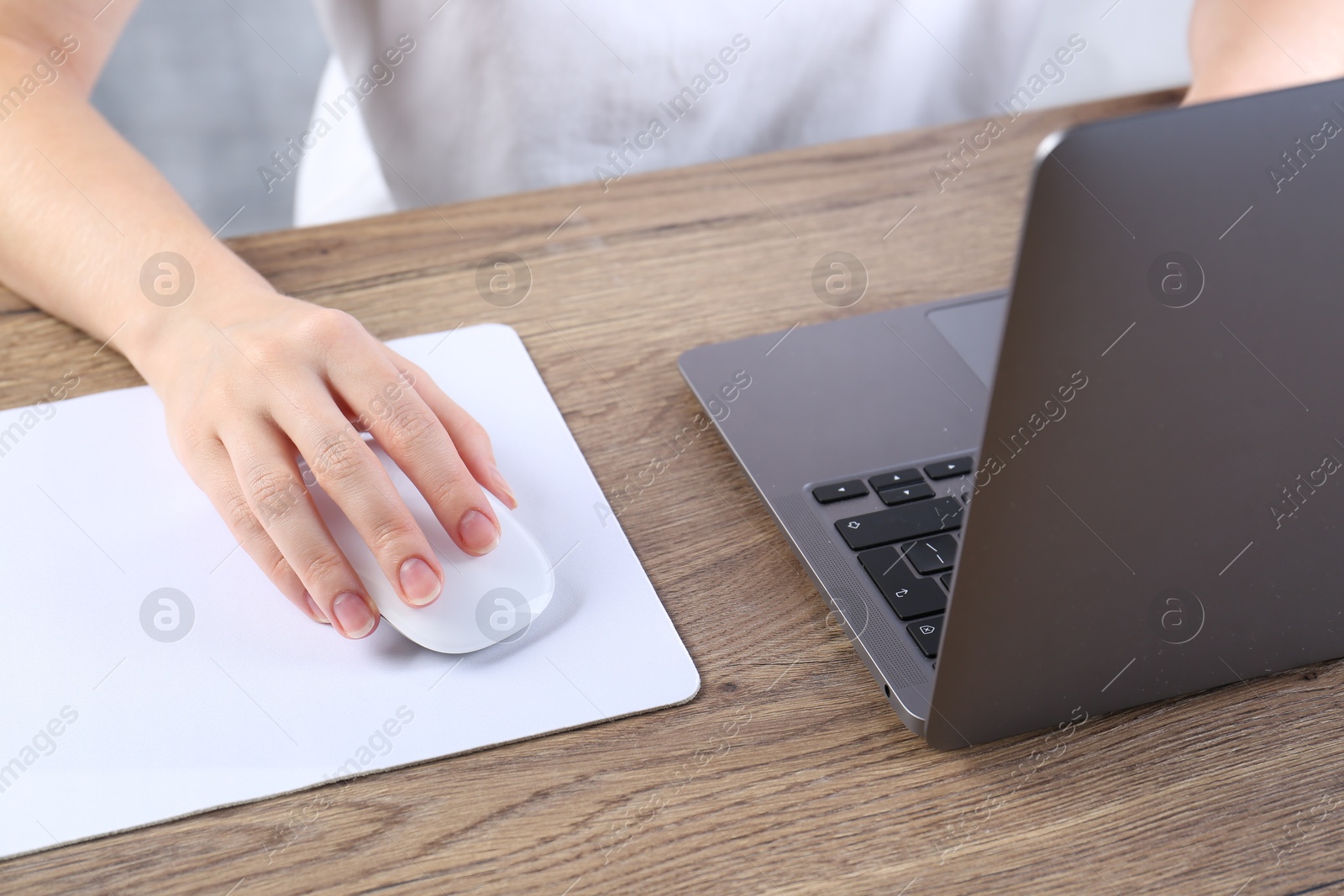 Photo of Woman using computer mouse while working with laptop at wooden table, closeup