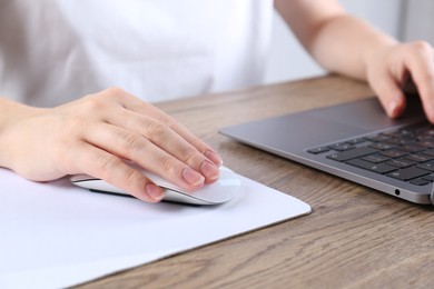 Photo of Woman using computer mouse while working with laptop at wooden table, closeup