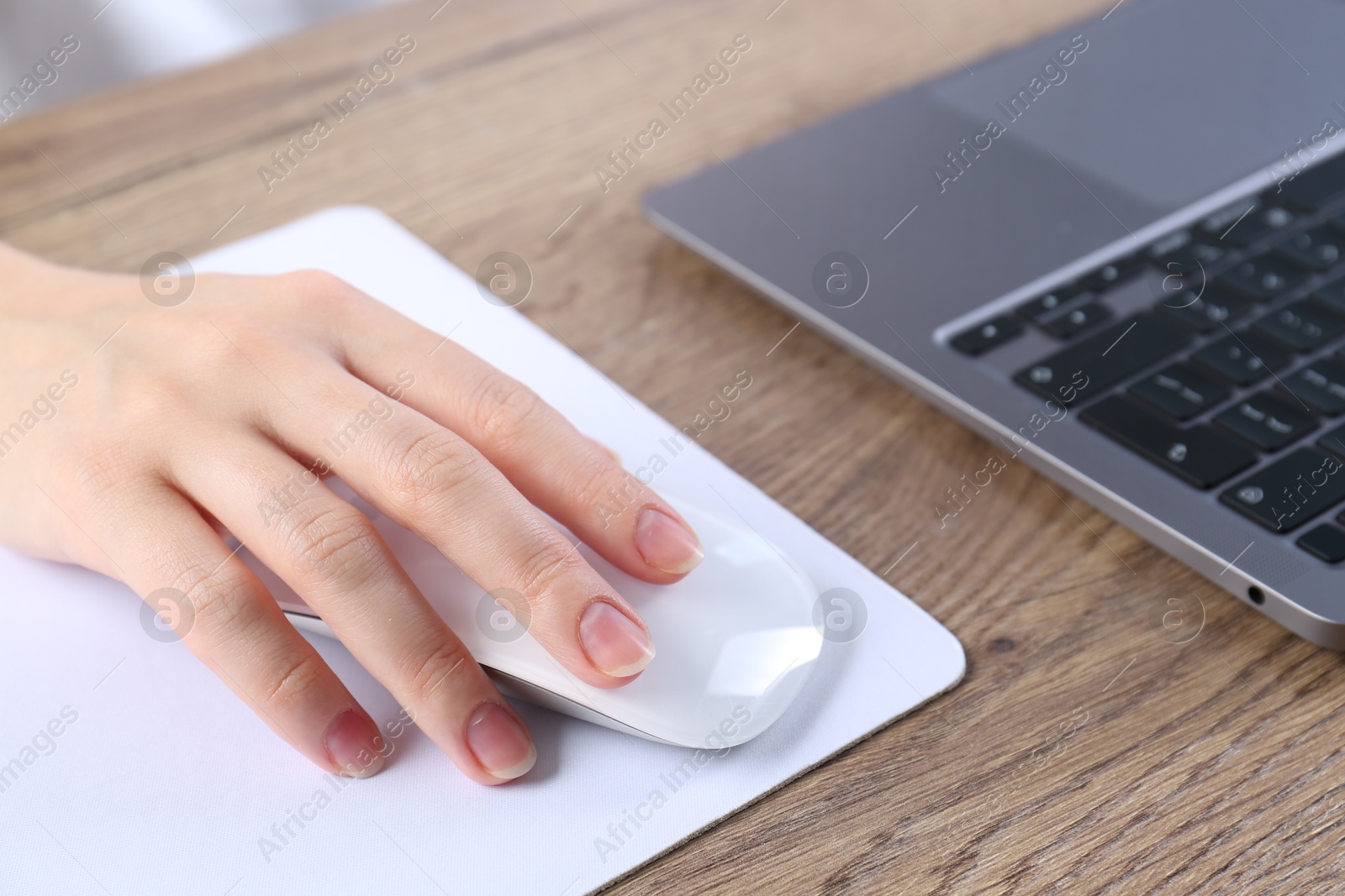 Photo of Woman using computer mouse while working with laptop at wooden table, closeup