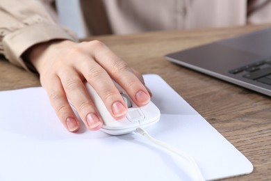 Photo of Woman using computer mouse while working with laptop at wooden table, closeup