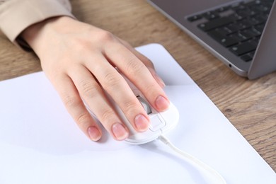 Photo of Woman using computer mouse while working with laptop at wooden table, closeup