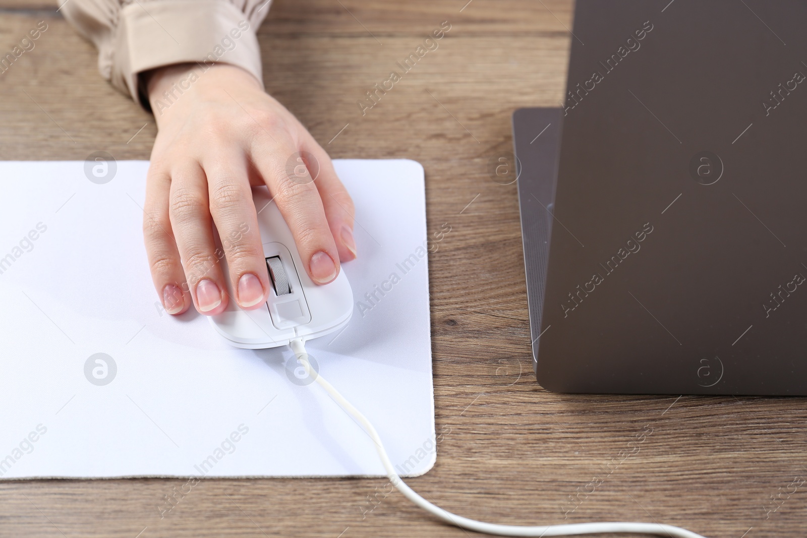 Photo of Woman using computer mouse while working with laptop at wooden table, closeup