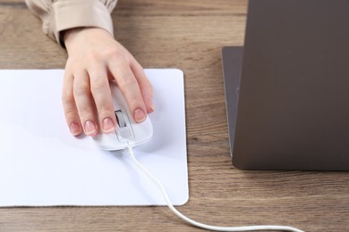 Photo of Woman using computer mouse while working with laptop at wooden table, closeup