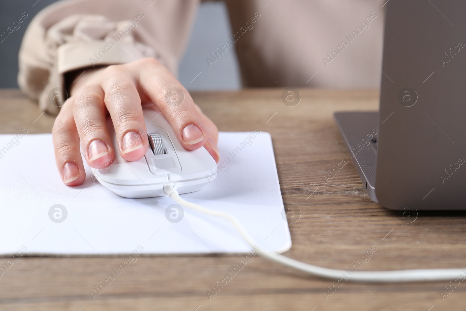 Photo of Woman using computer mouse while working with laptop at wooden table, closeup