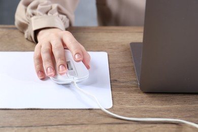 Photo of Woman using computer mouse while working with laptop at wooden table, closeup