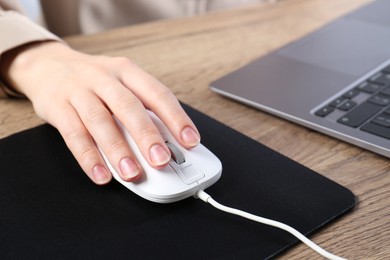 Photo of Woman using computer mouse while working with laptop at wooden table, closeup