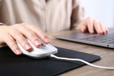 Photo of Woman using computer mouse while working with laptop at wooden table, closeup