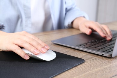 Photo of Woman using computer mouse while working with laptop at wooden table, closeup