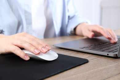 Photo of Woman using computer mouse while working with laptop at wooden table, closeup