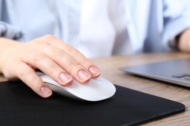 Photo of Woman using computer mouse while working with laptop at wooden table, closeup