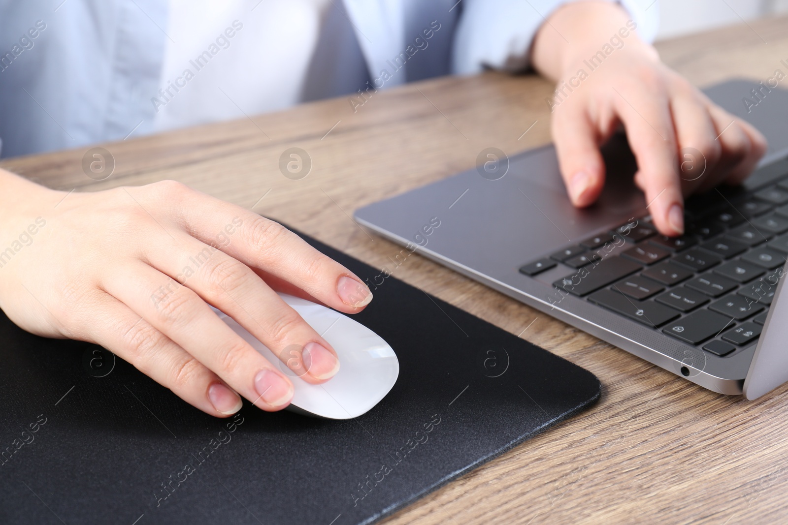 Photo of Woman using computer mouse while working with laptop at wooden table, closeup