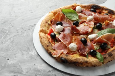 Photo of Tasty pizza with cured ham, olives, mozzarella cheese, sun-dried tomato and basil on gray textured table. Space for text