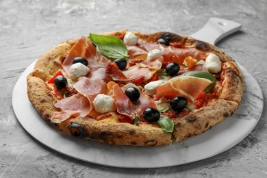 Tasty pizza with cured ham, olives, mozzarella cheese, sun-dried tomato and basil on gray textured table