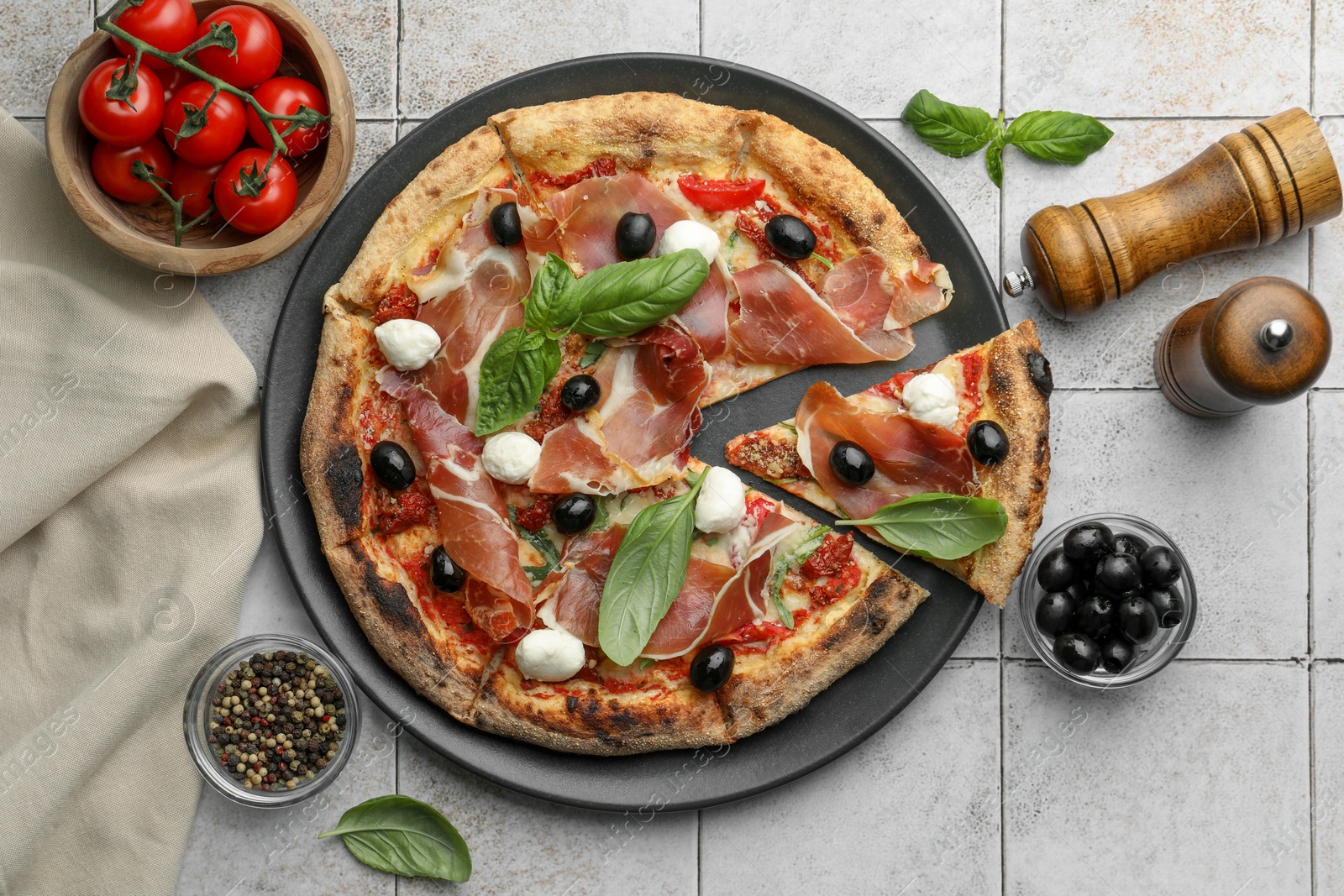 Photo of Tasty pizza with cured ham, olives, mozzarella cheese, tomatoes and basil on light tiled table, flat lay