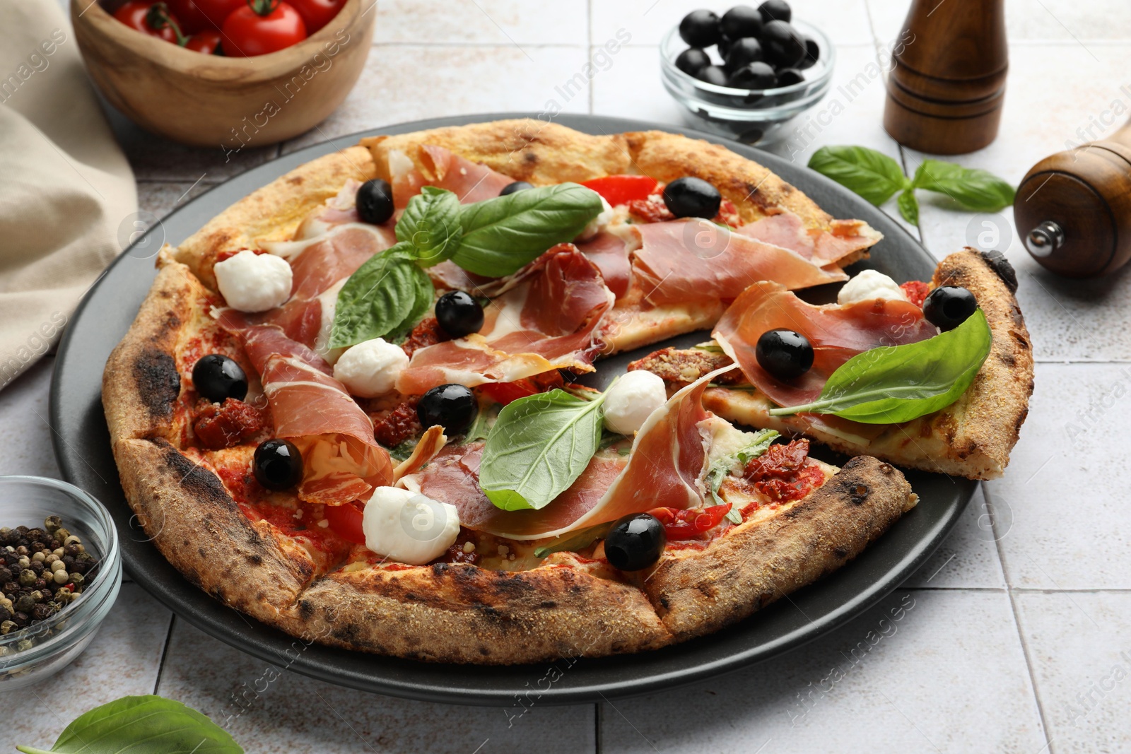 Photo of Tasty pizza with cured ham, olives, mozzarella cheese, sun-dried tomato and basil on light tiled table, closeup