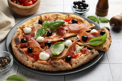 Tasty pizza with cured ham, olives, mozzarella cheese, sun-dried tomato and basil on light tiled table, closeup