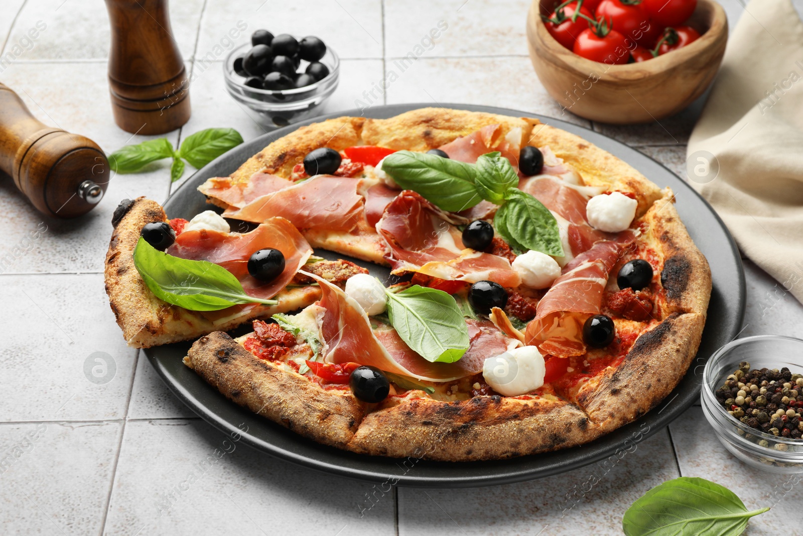 Photo of Tasty pizza with cured ham, olives, mozzarella cheese, tomatoes and basil on light tiled table, closeup