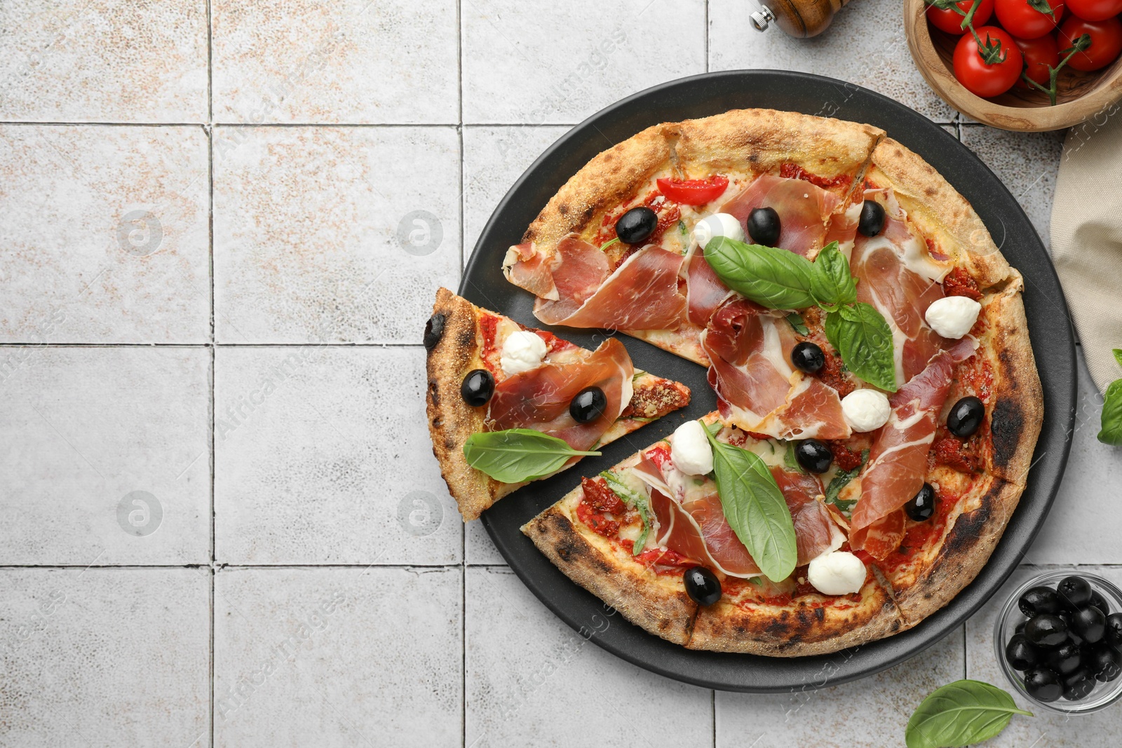 Photo of Tasty pizza with cured ham, olives, mozzarella cheese, tomatoes and basil on light tiled table, top view. Space for text