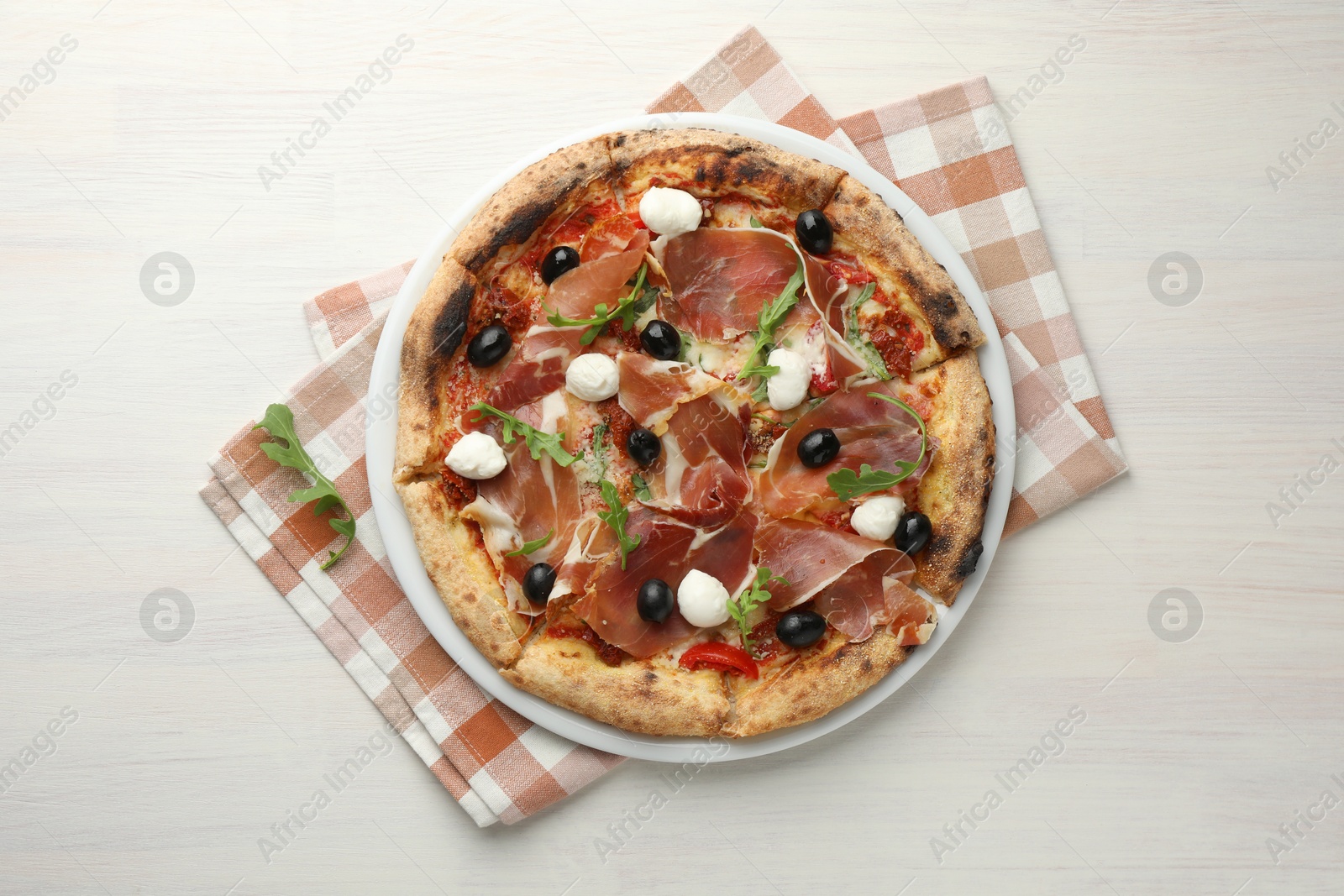 Photo of Tasty pizza with cured ham, olives, mozzarella cheese, sun-dried tomato and arugula on light wooden table, top view