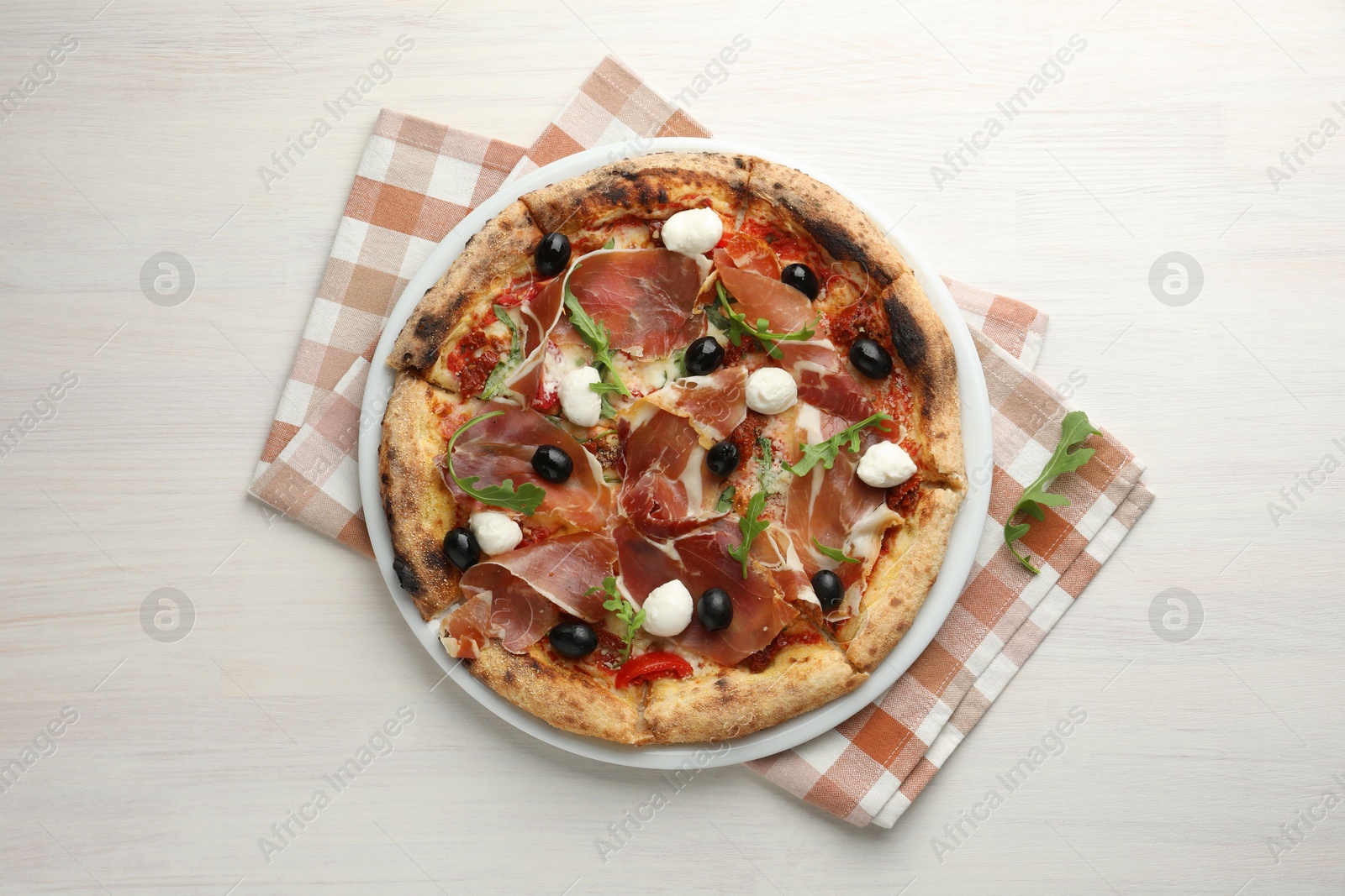 Photo of Tasty pizza with cured ham, olives, mozzarella cheese, sun-dried tomato and arugula on light wooden table, top view