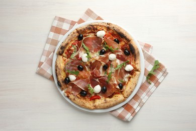 Tasty pizza with cured ham, olives, mozzarella cheese, sun-dried tomato and arugula on light wooden table, top view