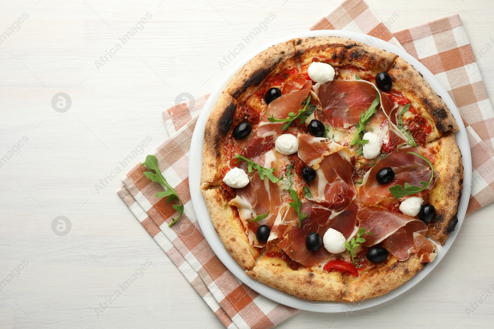 Photo of Tasty pizza with cured ham, olives, mozzarella cheese, sun-dried tomato and arugula on light wooden table, top view. Space for text