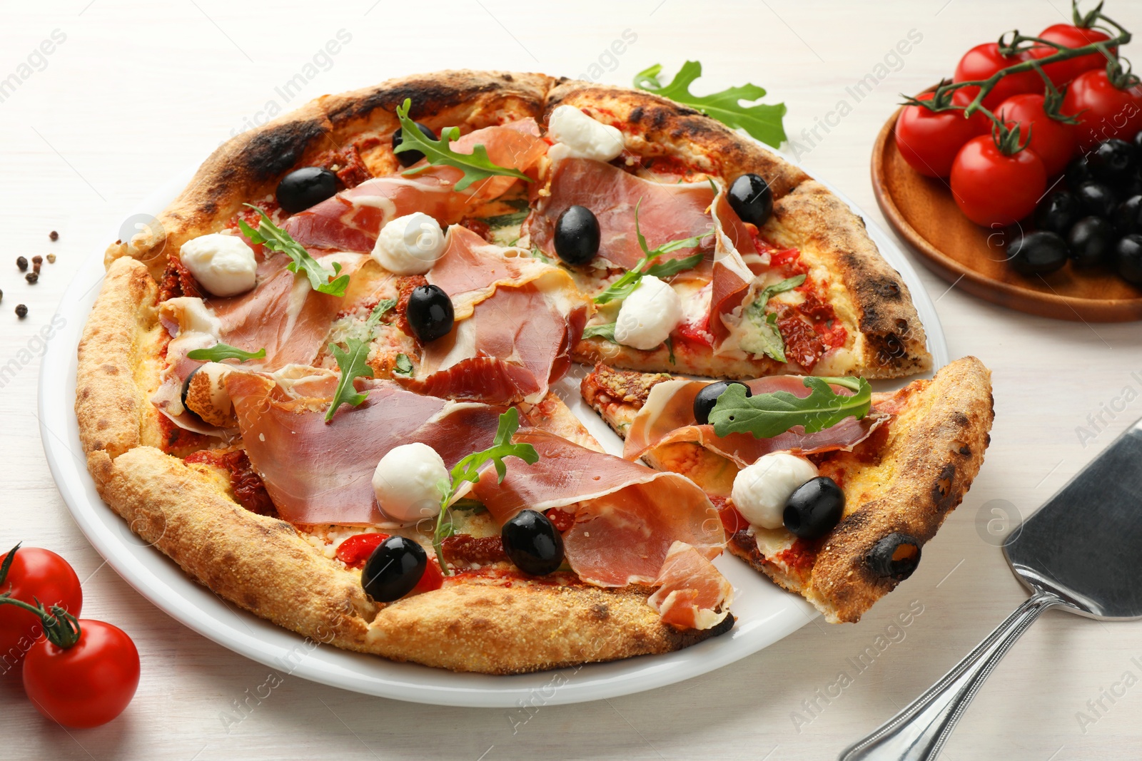 Photo of Tasty pizza with cured ham, olives, mozzarella cheese, tomatoes and arugula on light wooden table, closeup