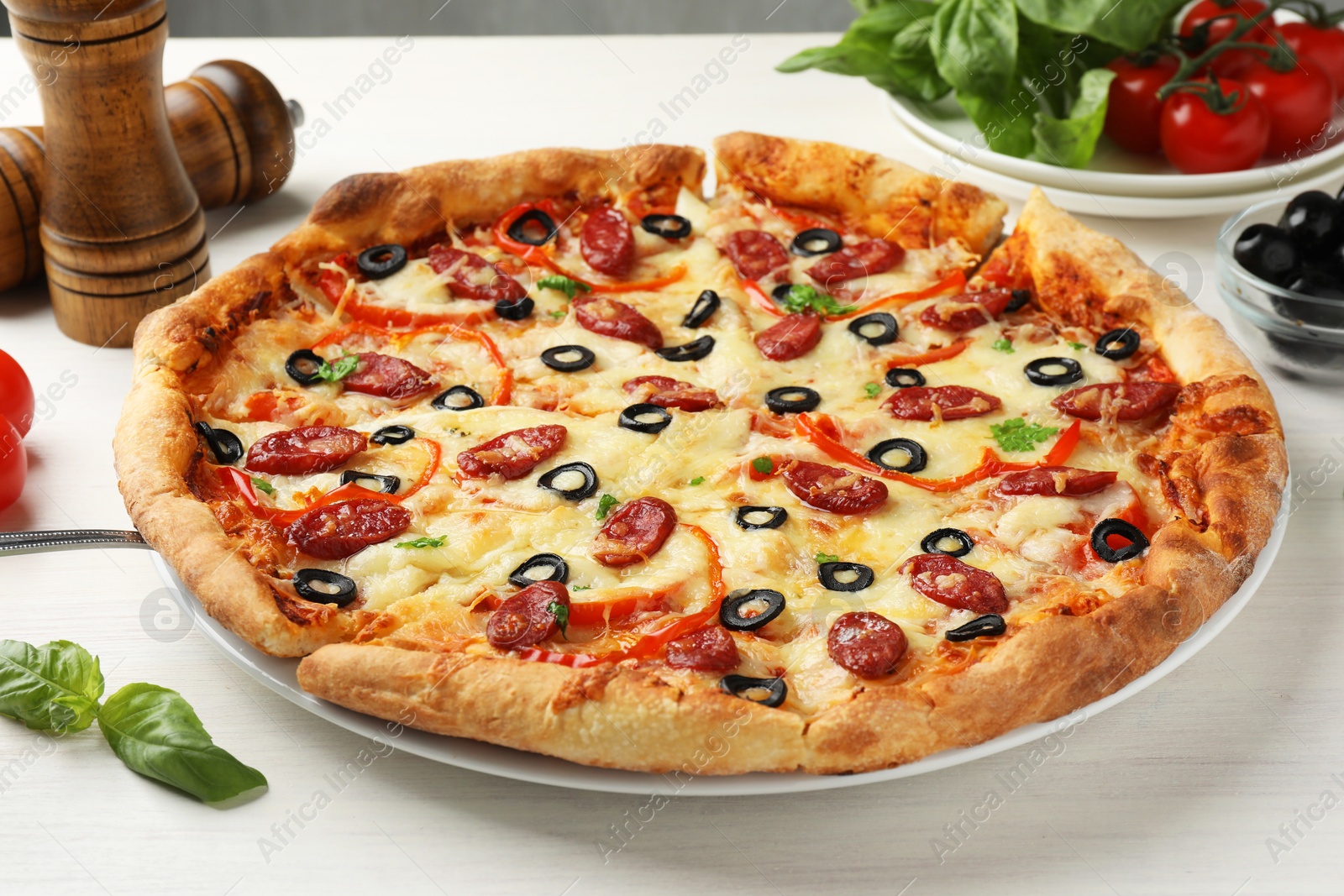 Photo of Tasty pizza with smoked sausages, olives, pepper and parsley on light wooden table, closeup