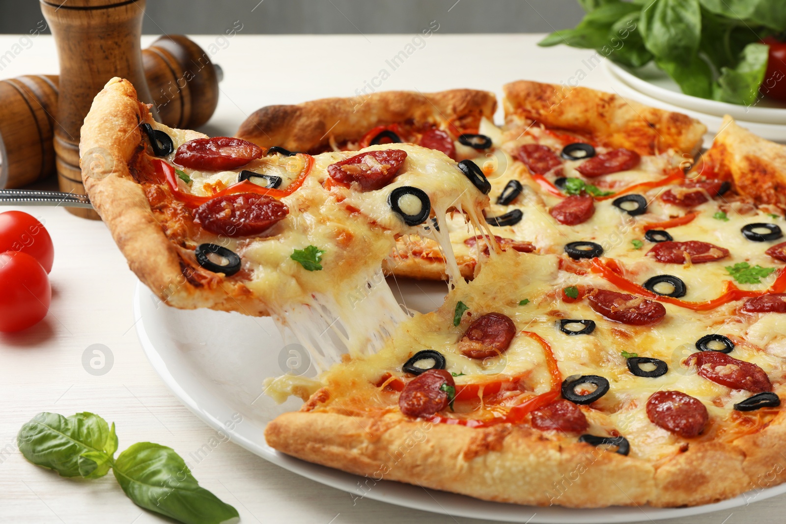 Photo of Taking piece of tasty pizza with smoked sausages, olives, pepper and parsley at light wooden table, closeup