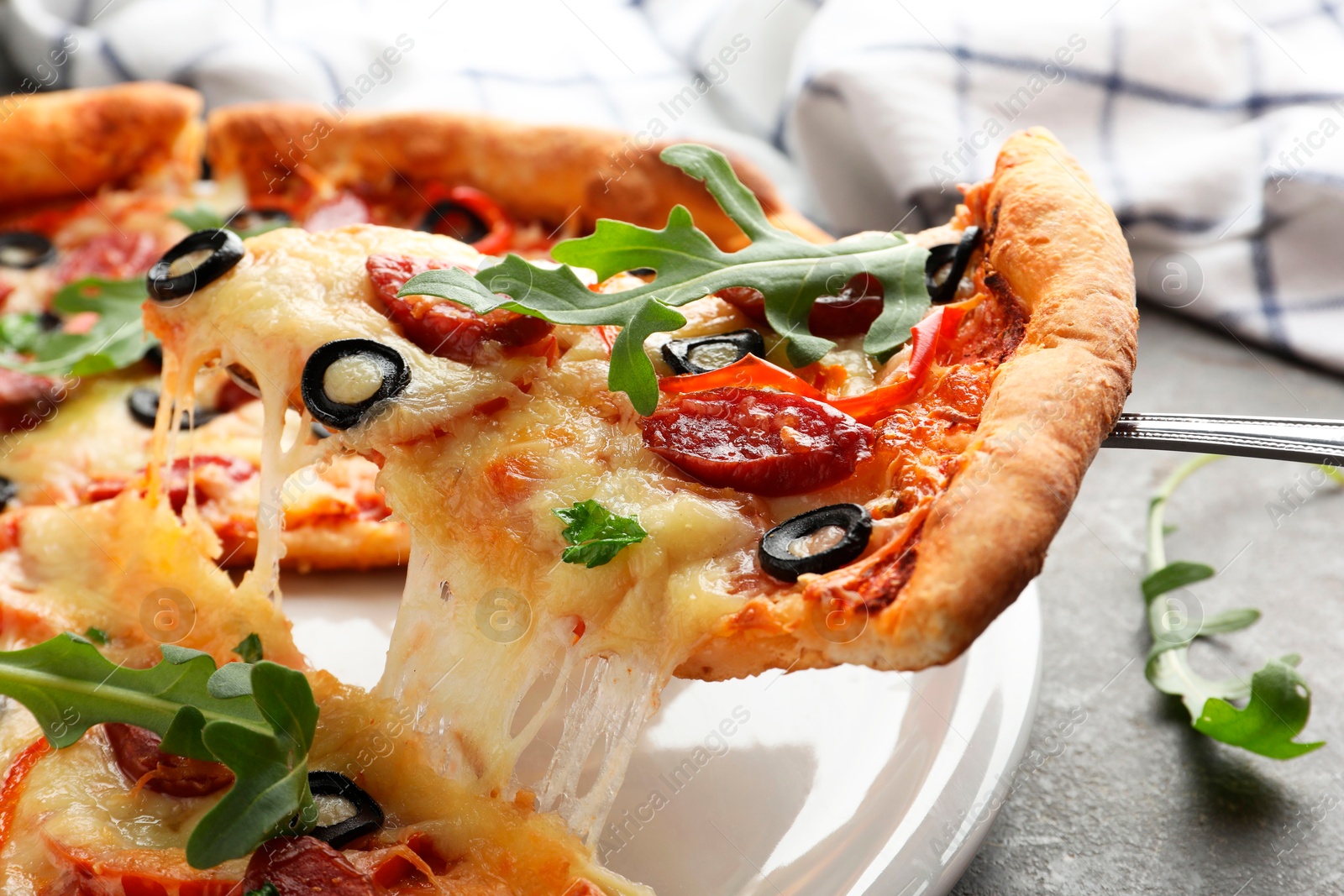 Photo of Taking piece of tasty pizza with smoked sausages, olives, pepper and parsley at gray table, closeup