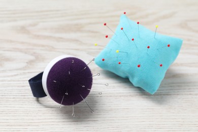 Pincushions with sewing needles on white wooden table