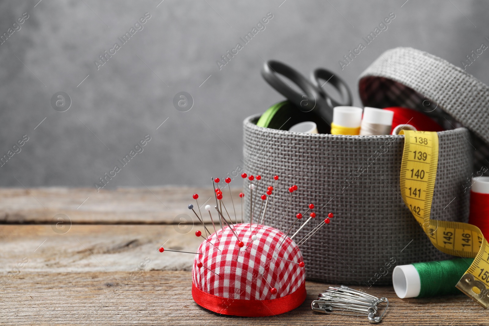 Photo of Checkered pincushion with pins and other sewing tools on wooden table