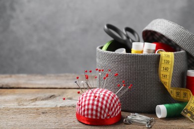 Checkered pincushion with pins and other sewing tools on wooden table