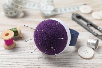 Photo of Blue pincushion with pins and other sewing tools on light wooden table, closeup