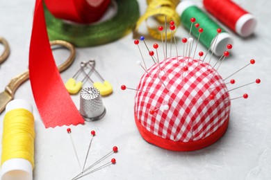 Photo of Checkered pincushion with pins and other sewing tools on grey table