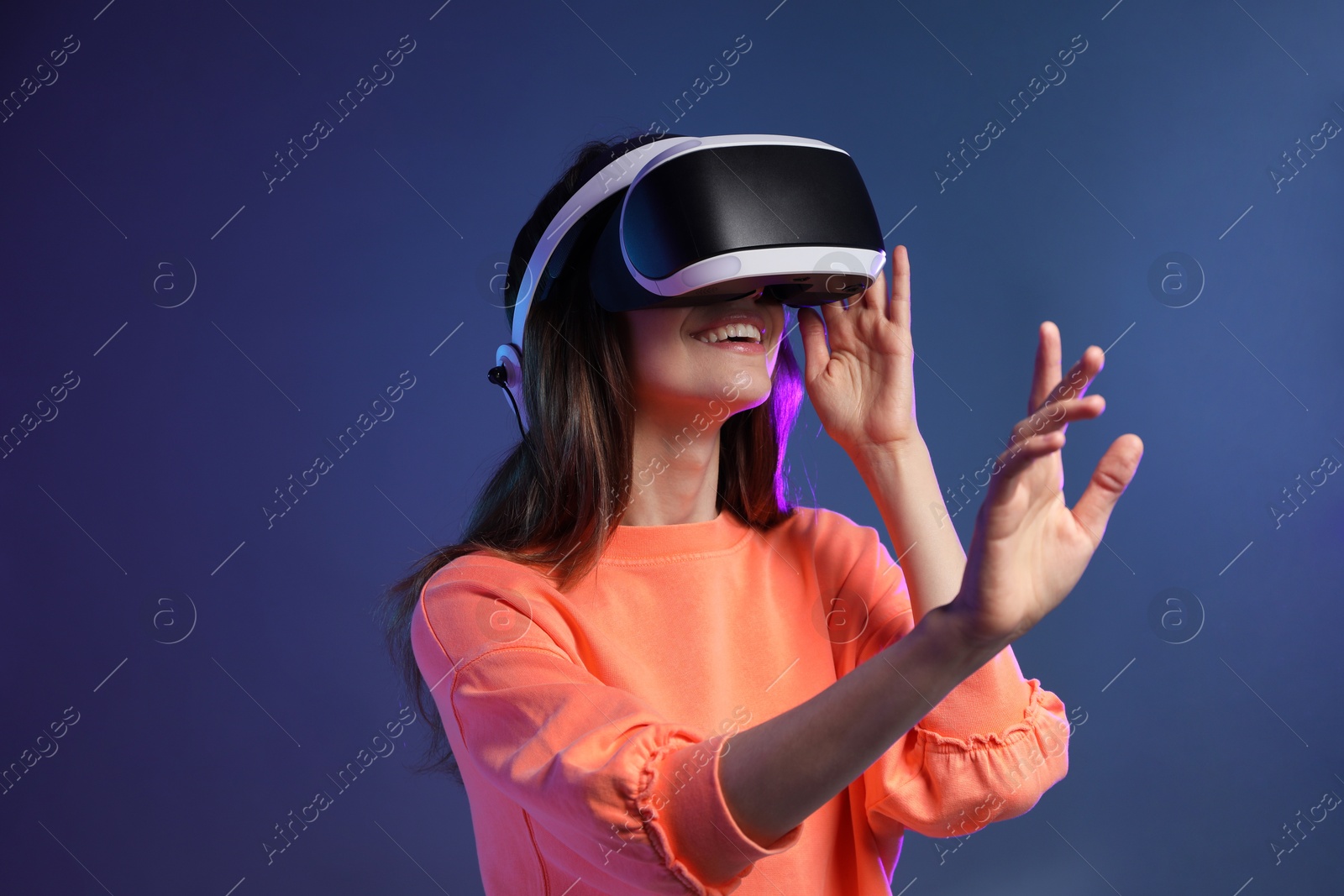 Photo of Smiling woman using virtual reality headset on dark blue background