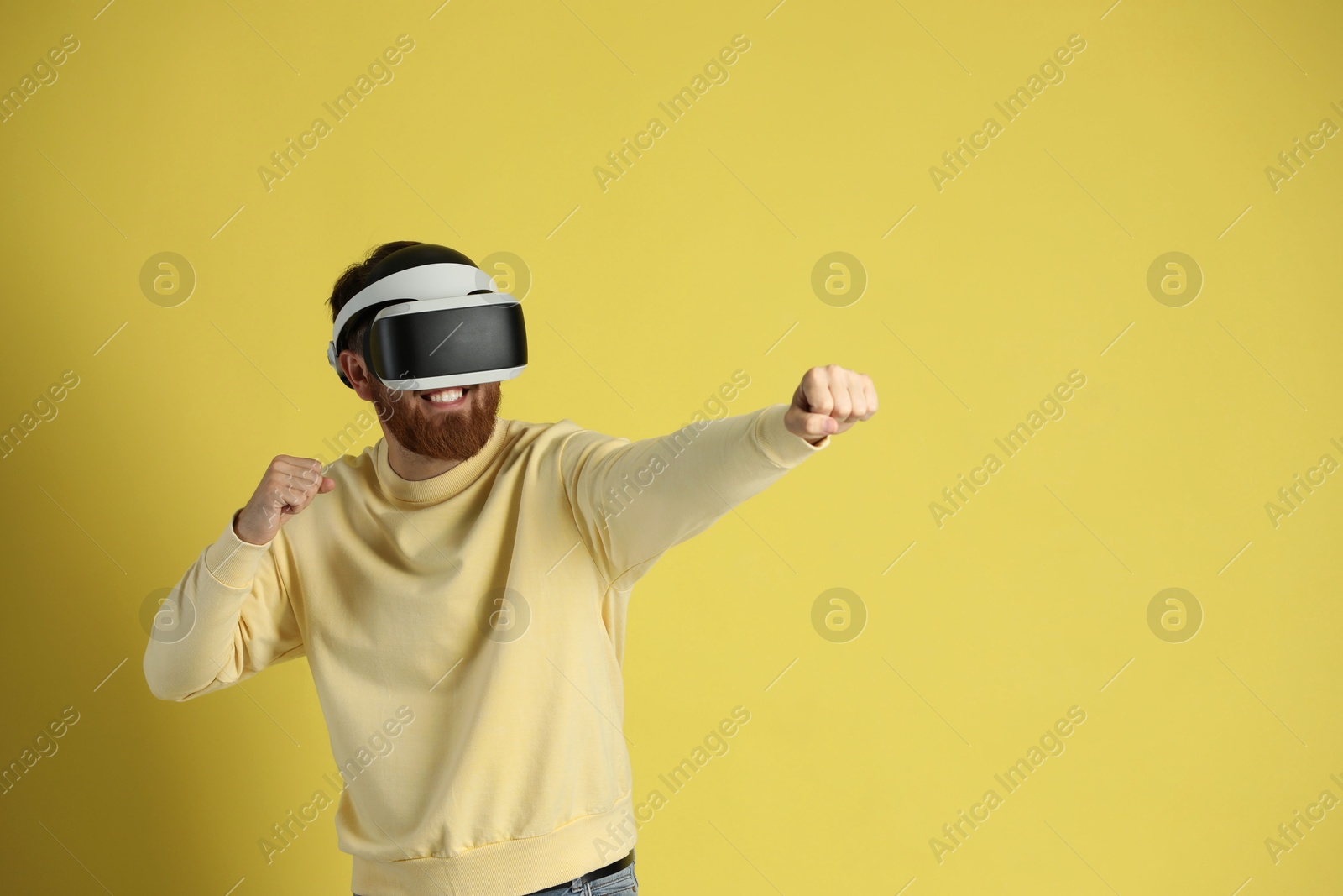 Photo of Happy man using virtual reality headset on pale yellow background. Space for text