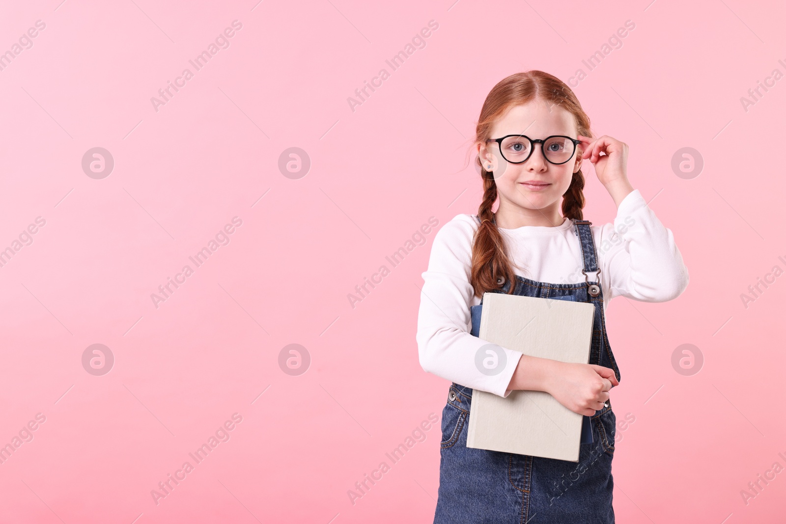 Photo of Cute little girl with book on pink background. Space for text