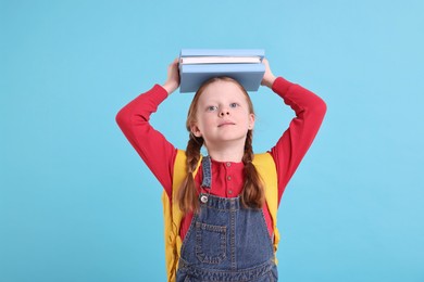 Photo of Cute little girl with stack of books on light blue background