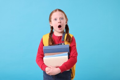 Photo of Surprised girl with stack of books on light blue background