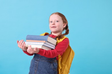 Photo of Smiling girl with stack of books on light blue background. Space for text