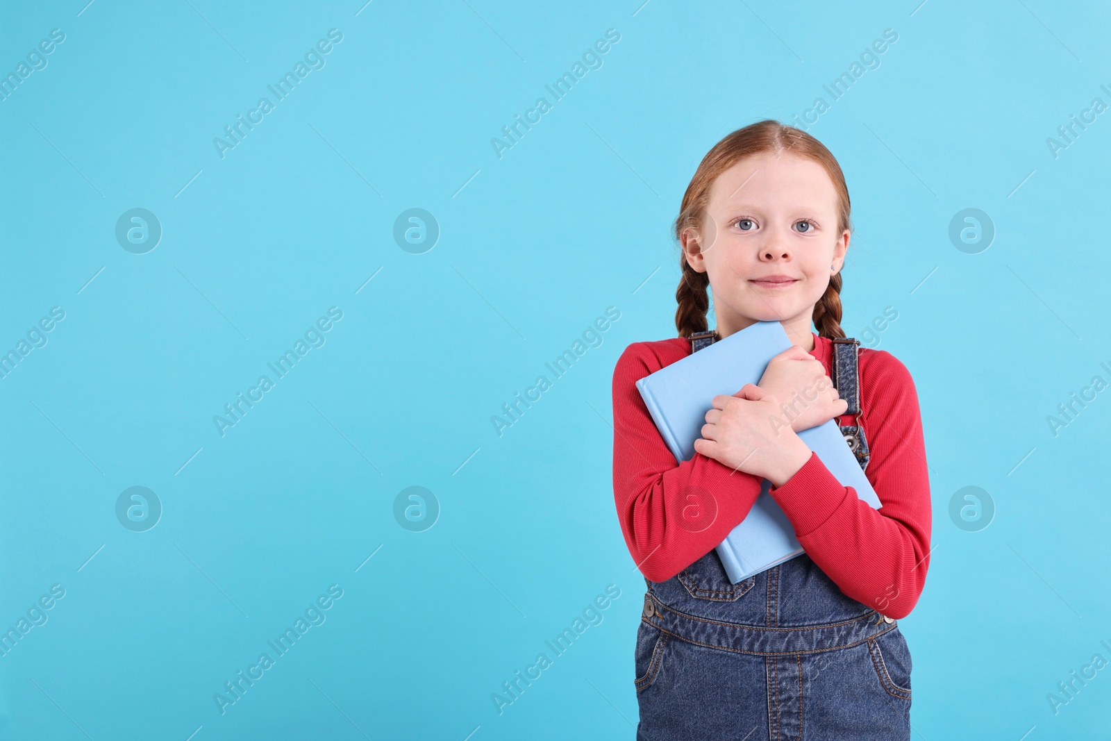 Photo of Cute little girl with book on light blue background. Space for text