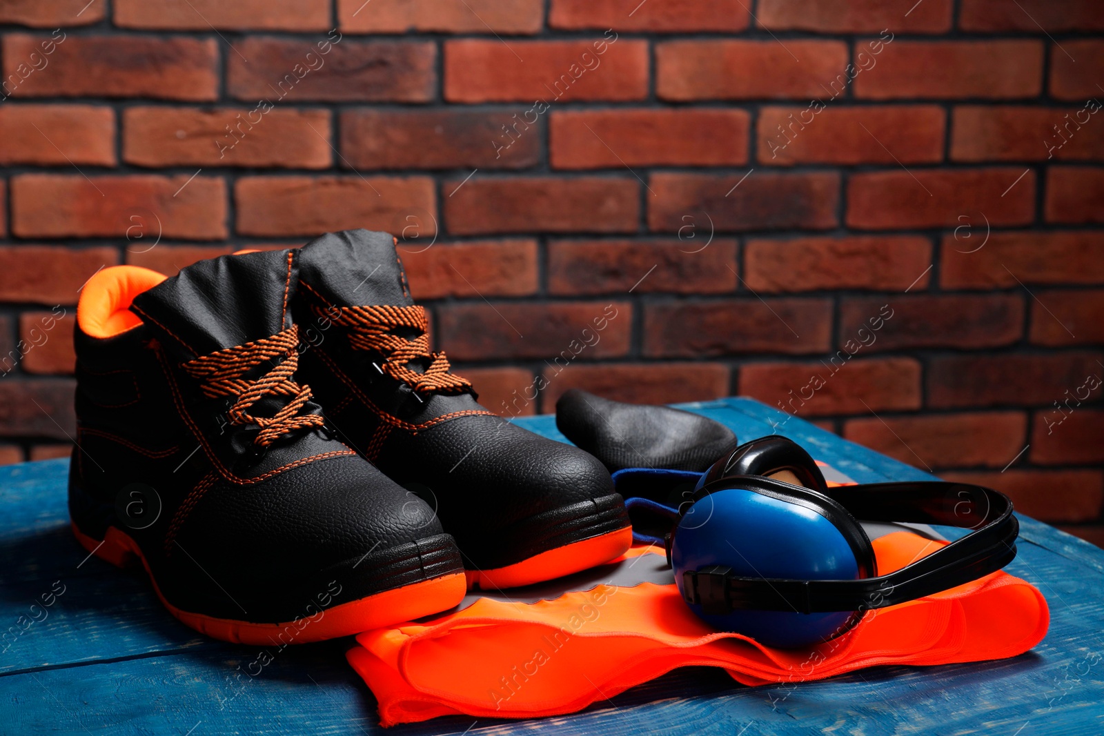Photo of Pair of working boots, reflective vest and earmuffs on blue wooden surface