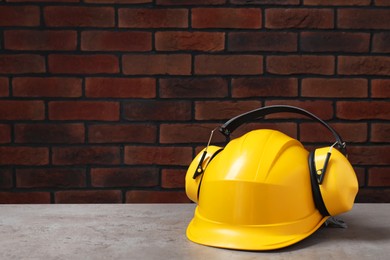 Photo of Hard hat and earmuffs on grey surface. Space for text