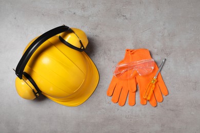 Photo of Hard hat, protective gloves, earmuffs, goggles and screwdriver on grey surface, flat lay